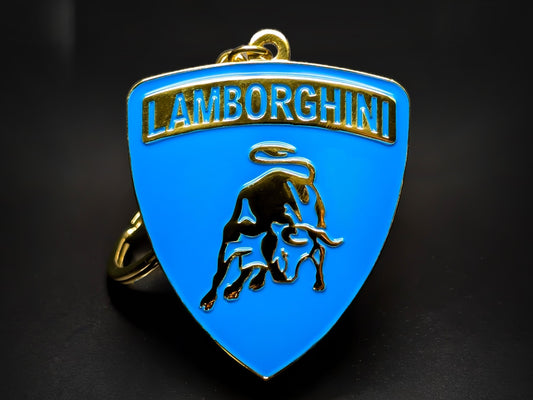 Shield-shaped blue and gold Lamborghini metal keychain with a golden bull logo and the "Lamborghini" wordmark.