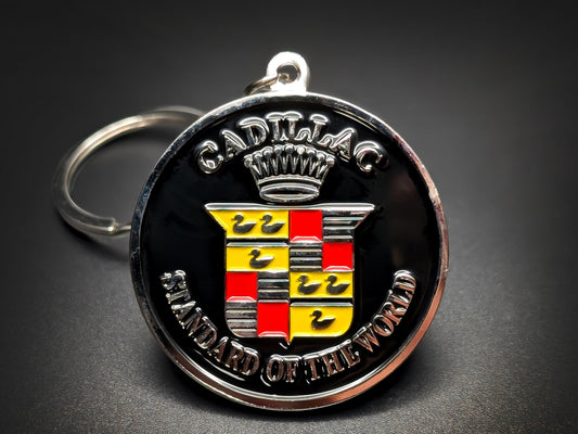 Round black and silver Cadillac double-sided metal keychain with the coat of arms logo and "CADILLAC STANDARD OF THE WORLD" text.
