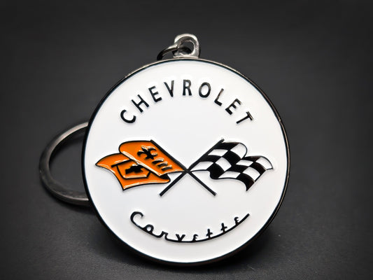 Round white metal Chevrolet Corvette double-sided keychain with two crossed racing flags, one orange and one checkered.