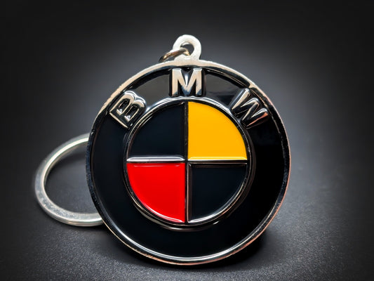 Round black and silver BMW double-sided metal keychain with a red, yellow, and black checkered logo and "BMW" text.