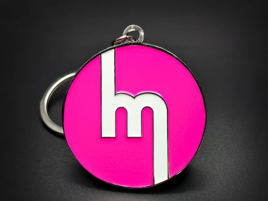 Round pink double-sided metal Mazda keychain with a stylized white "M" logo.