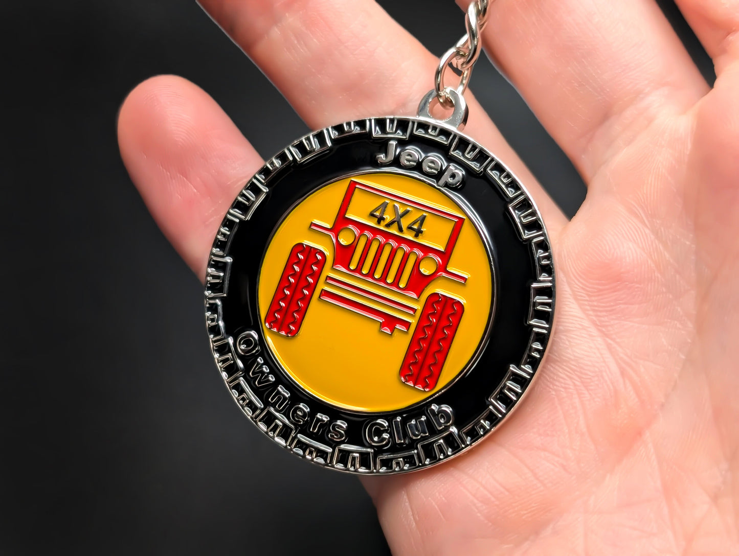A hand holding the Jeep Club badge keychain, demonstrating its solid construction and textured metal finish.