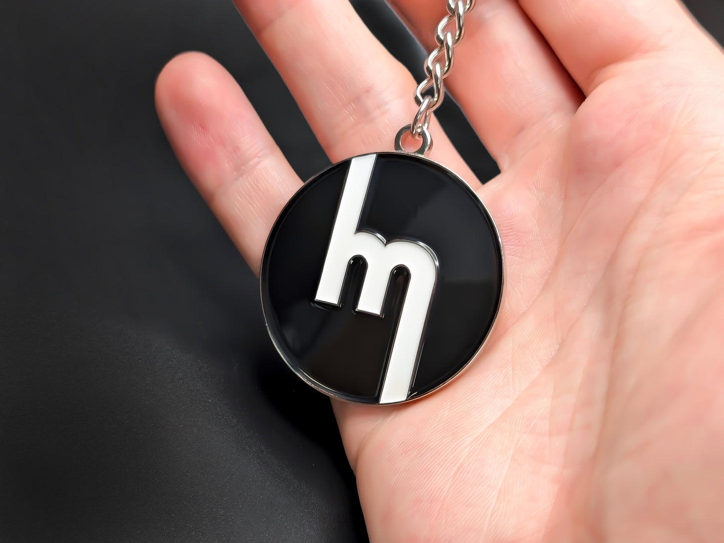 Hand holding a circular Mazda heritage enamel badge keychain to demonstrate the high-contrast design and premium finish.