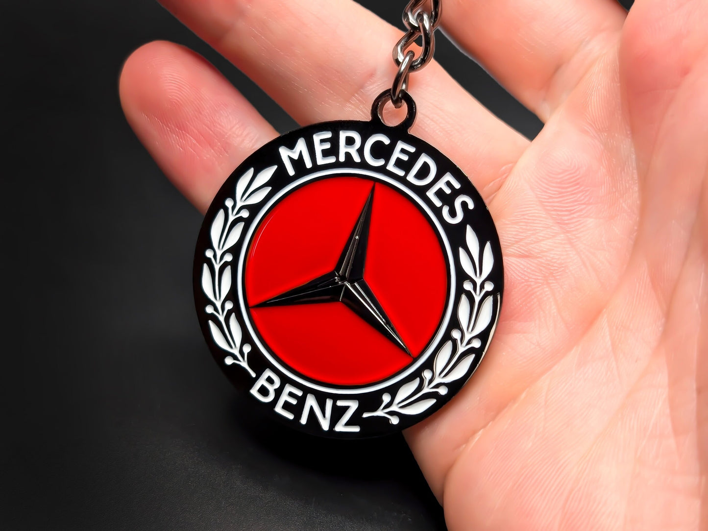 Hand holding a circular Mercedes-Benz heritage enamel badge keychain to demonstrate the high-contrast red and black design and premium finish.