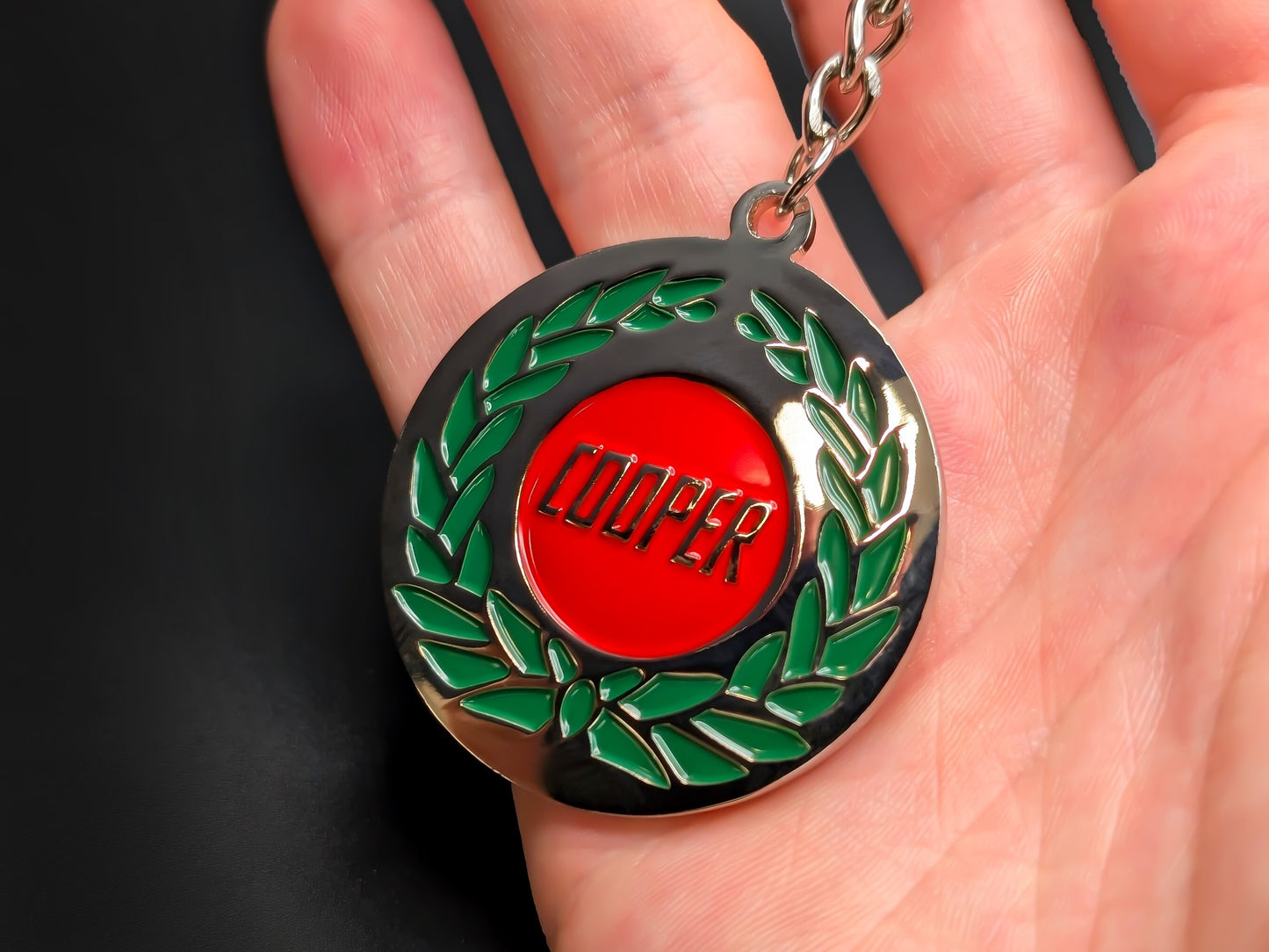 Hand holding a circular Mini Cooper enamel badge keychain to demonstrate the premium metallic weight and vibrant racing colors.