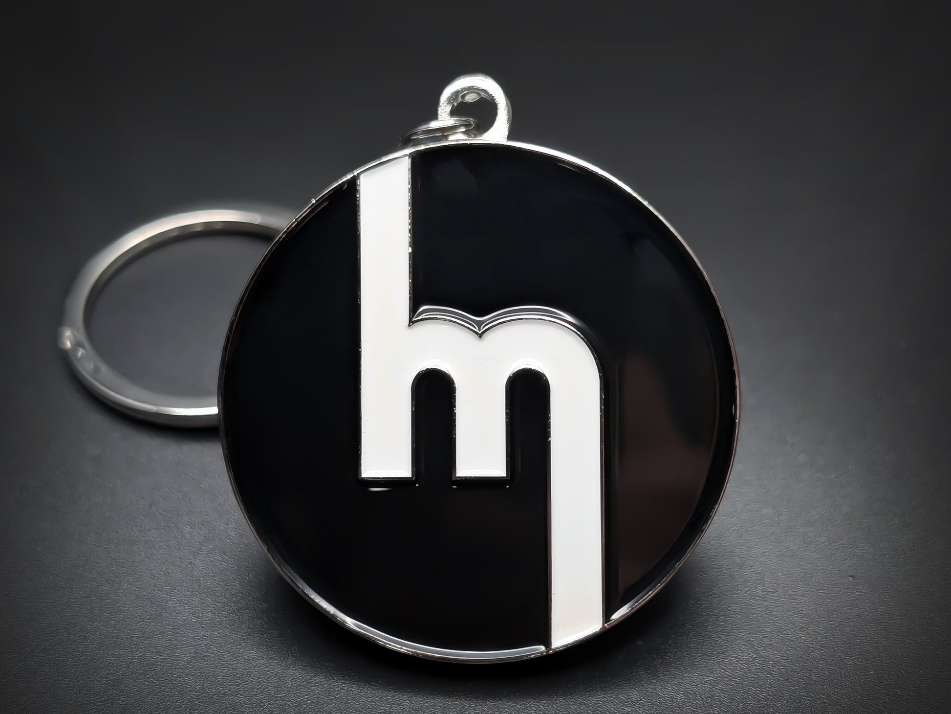 Round black double-sided metal Mazda keychain with a stylized white "M" logo.