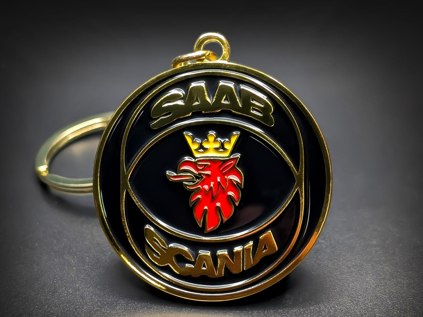 Round black, red, and gold Saab metal keychain with a griffin emblem and "SAAB SCANIA" text.