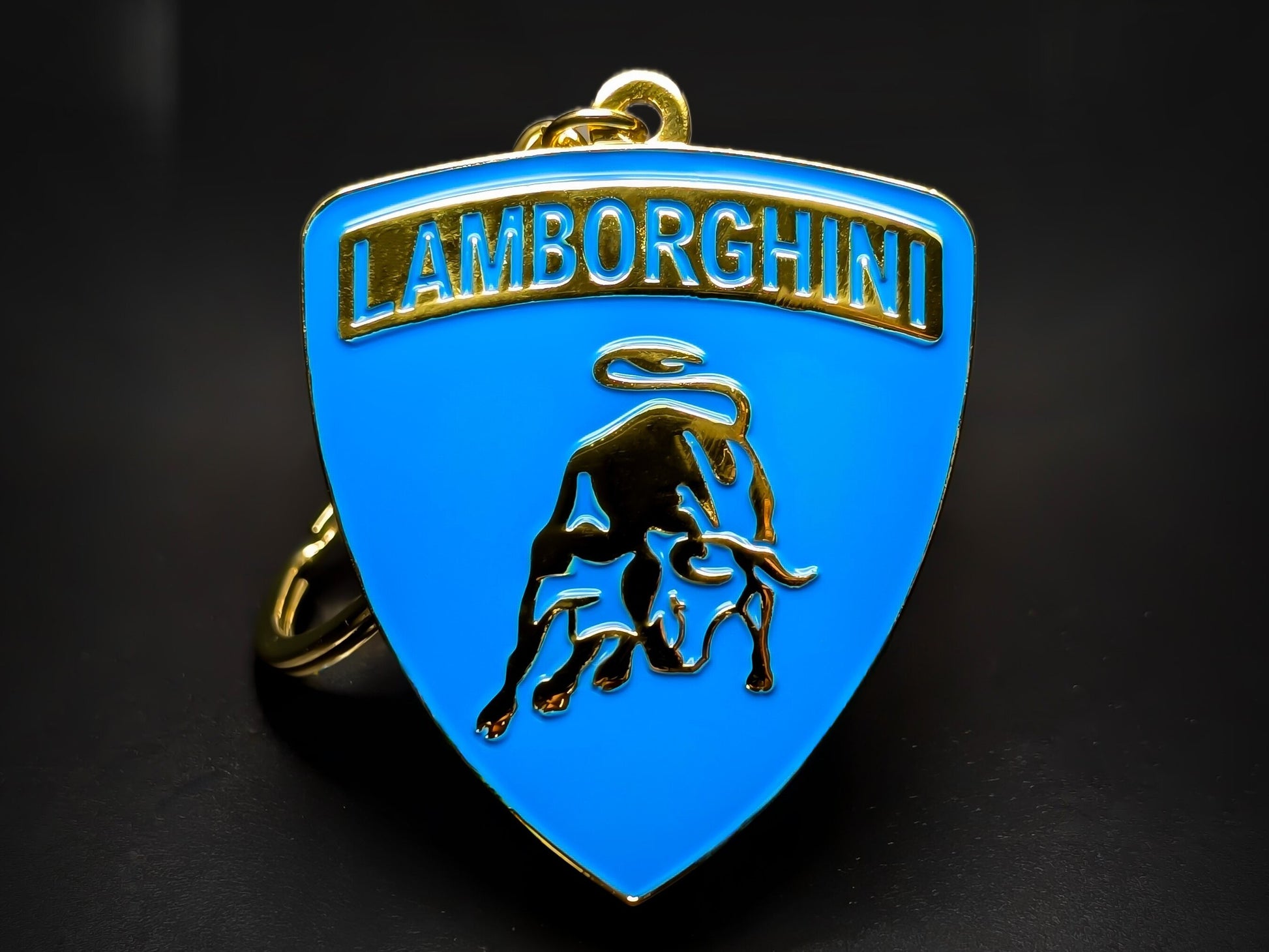 Shield-shaped blue and gold Lamborghini metal keychain with a golden bull logo and the "Lamborghini" wordmark.