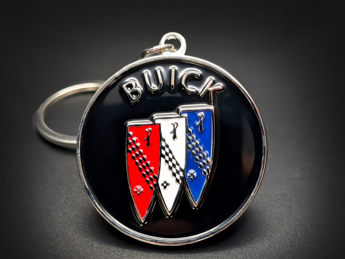 Round black and silver Buick metal keychain with three red, white, and blue tri-shields and "BUICK" text.