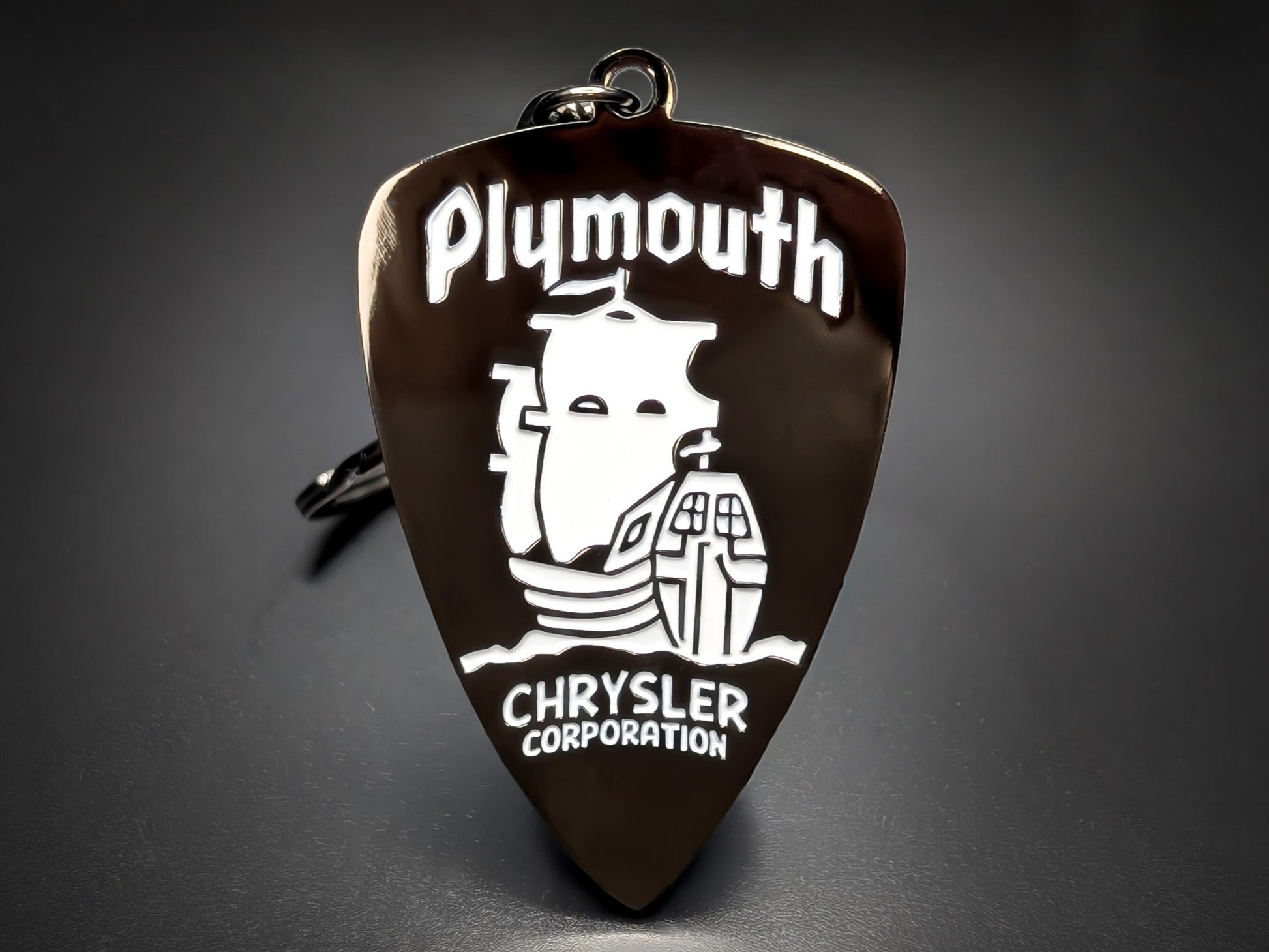 Silver Plymouth Chrysler keychain with a dark background and a classic logo featuring the Mayflower ship.