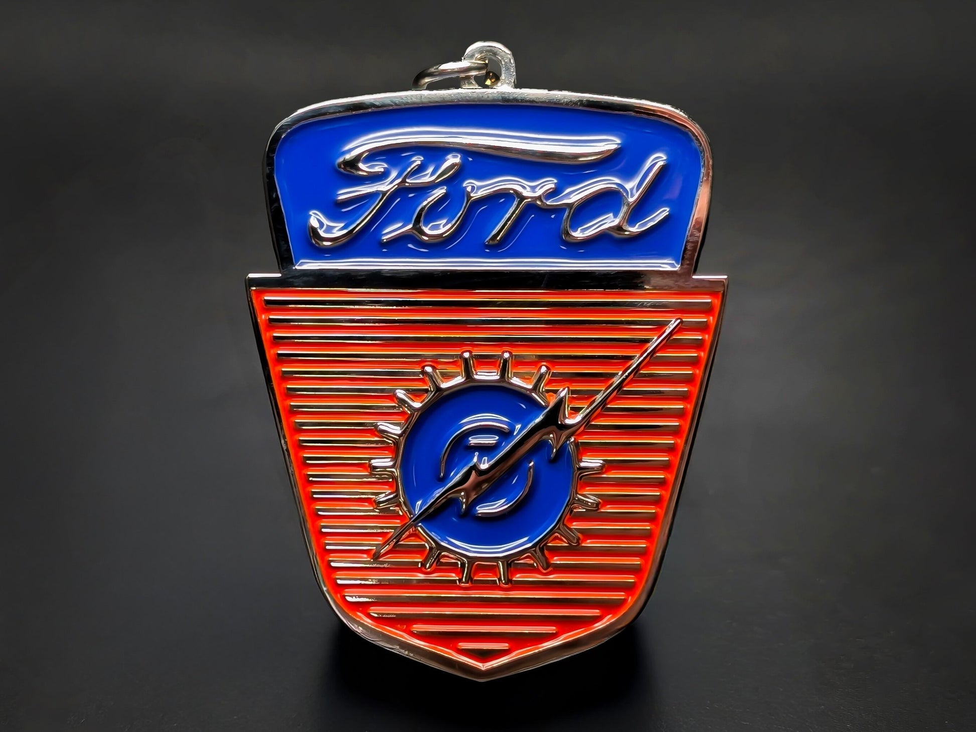 Blue and silver vintage Ford truck grille metal keychain with a orange pinstripe background and the classic Ford script emblem.