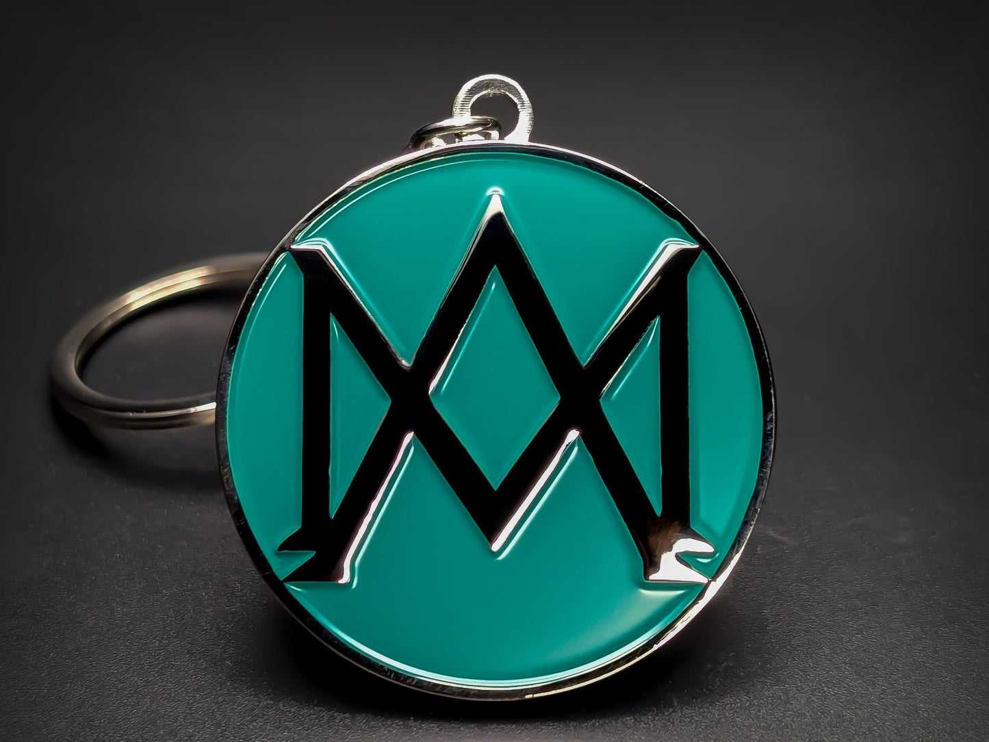 Round green and silver Aston Martin keychain with a large "M" shaped logo in the center.