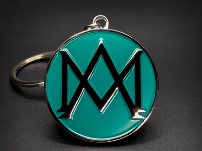 Round green and silver Aston Martin keychain with a large "M" shaped logo in the center.