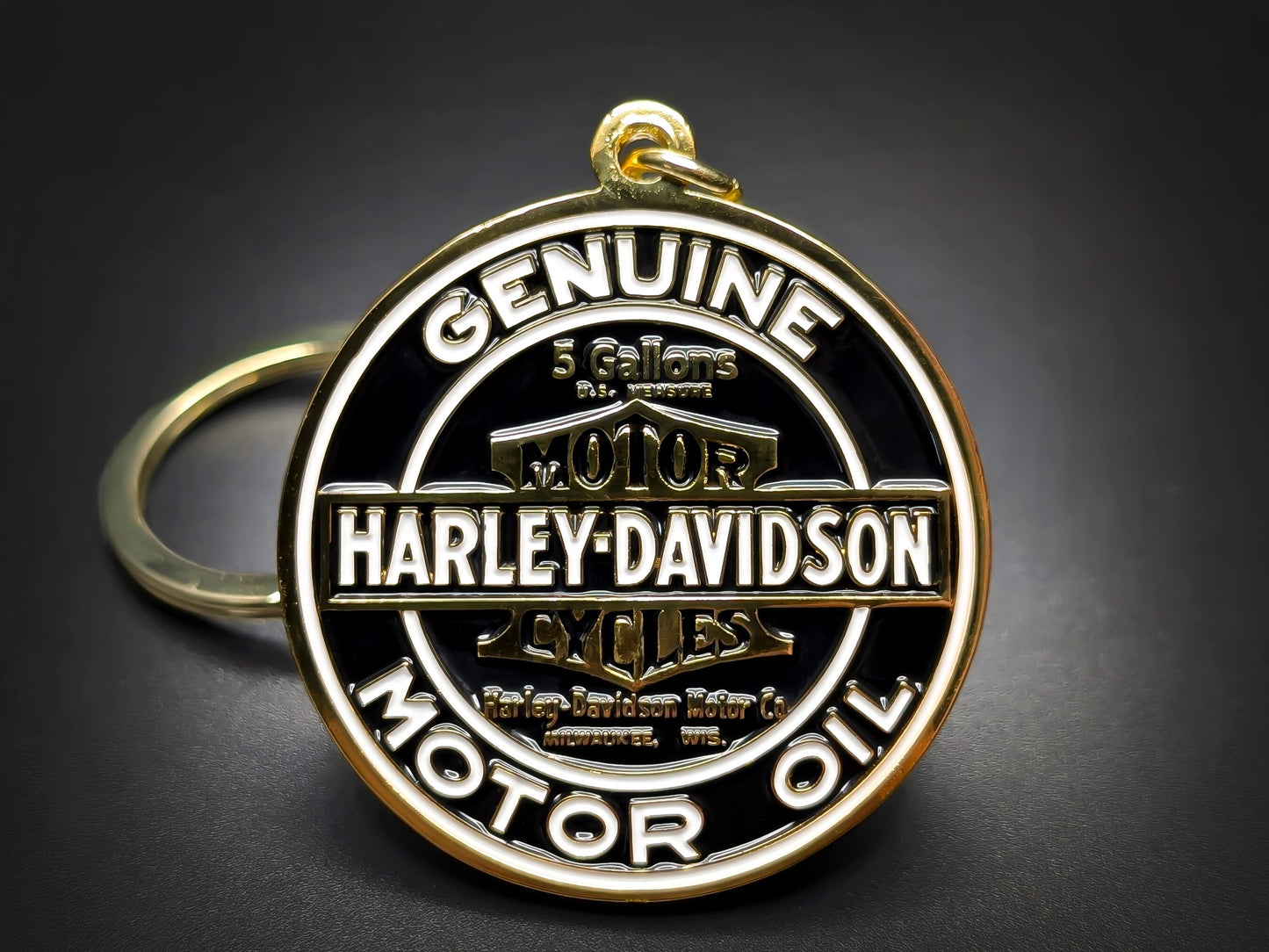 Round gold and black Harley-Davidson metal keychain with "GENUINE MOTOR OIL" and the classic bar and shield logo.
