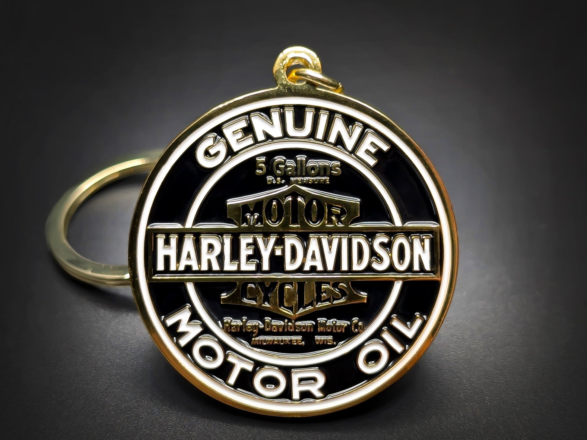 Round gold and black Harley-Davidson metal keychain with "GENUINE MOTOR OIL" and the classic bar and shield logo.