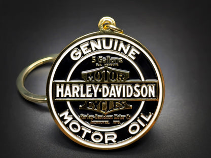 Round gold and black Harley-Davidson metal keychain with "GENUINE MOTOR OIL" and the classic bar and shield logo.