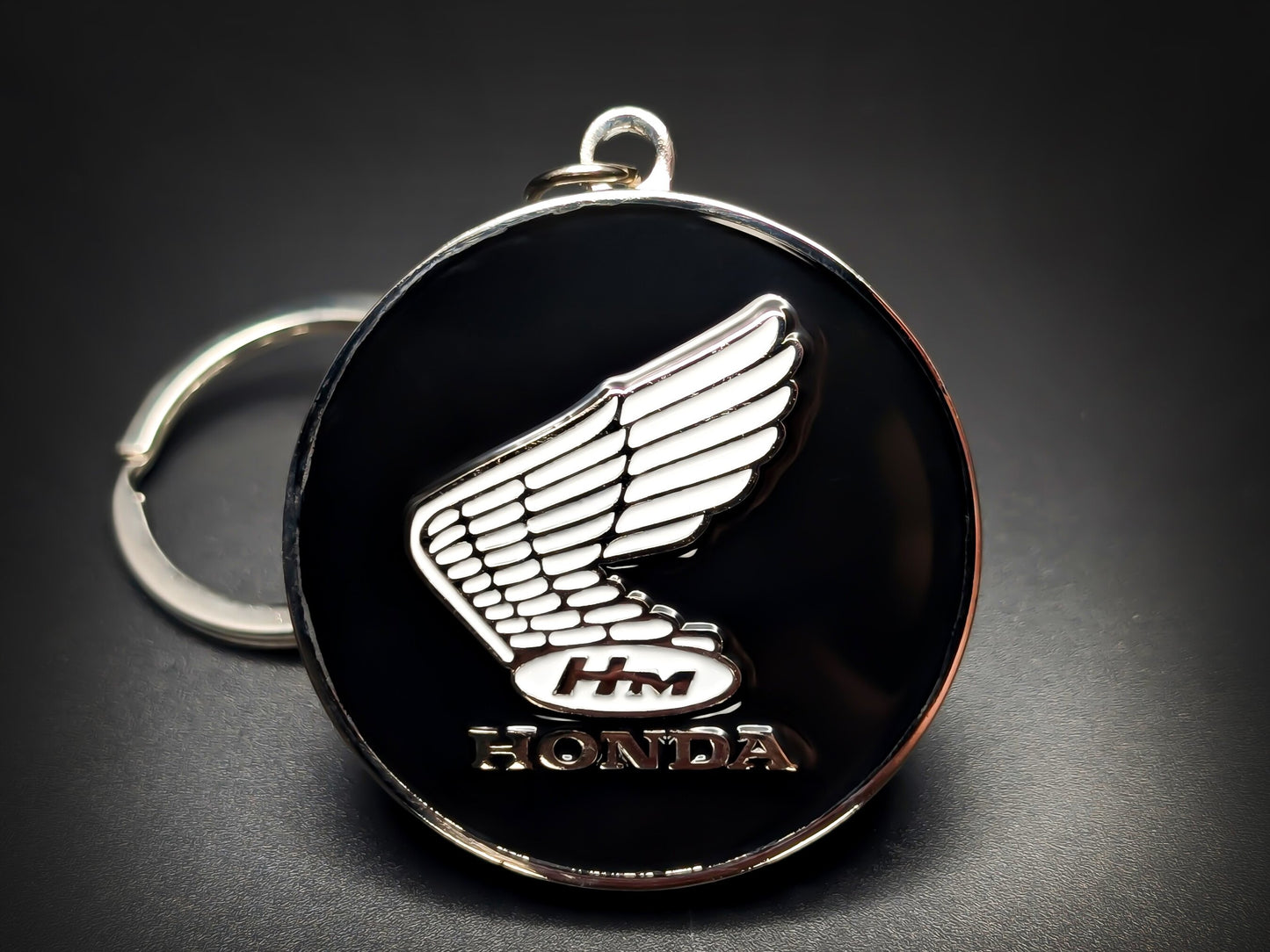 Round black and silver Honda keychain with a white winged logo and "HONDA" text.