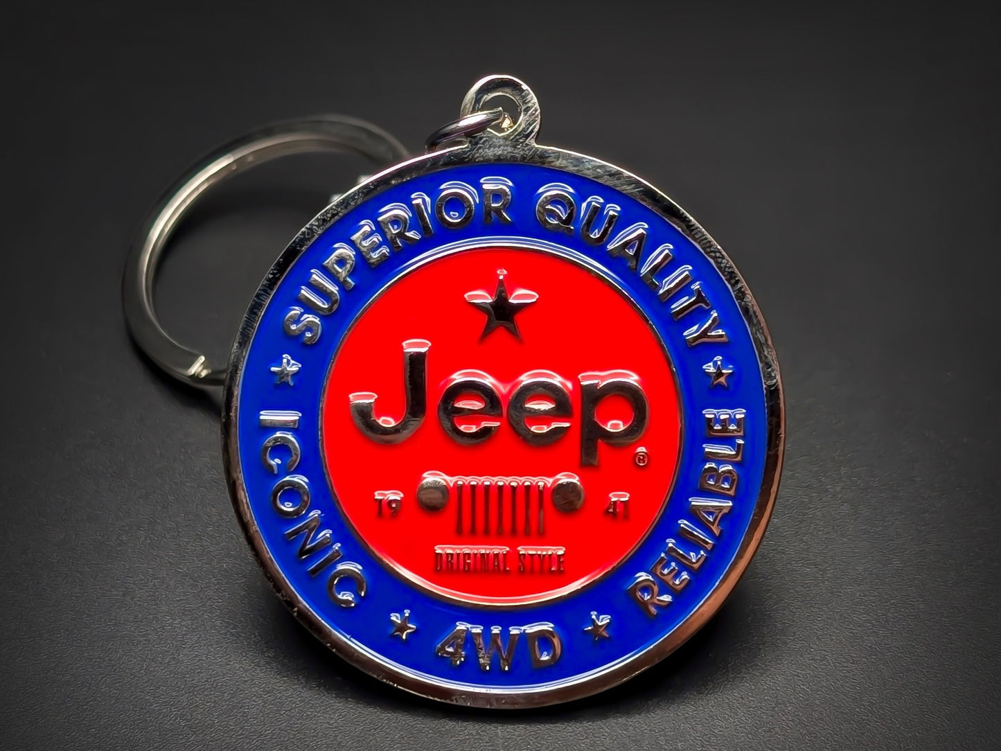 Round blue and red metal Jeep double-sided keychain with a classic grille logo and "SUPERIOR QUALITY ICONIC RELIABLE" text.