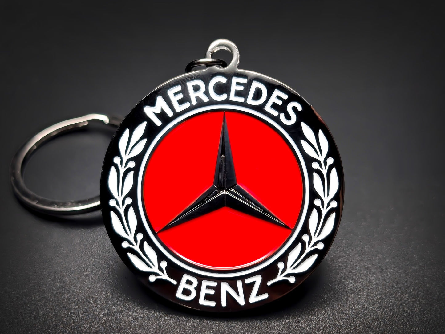 Round black metal Mercedes-Benz keychain with a red center, black three-pointed star, and white "MERCEDES BENZ" text.