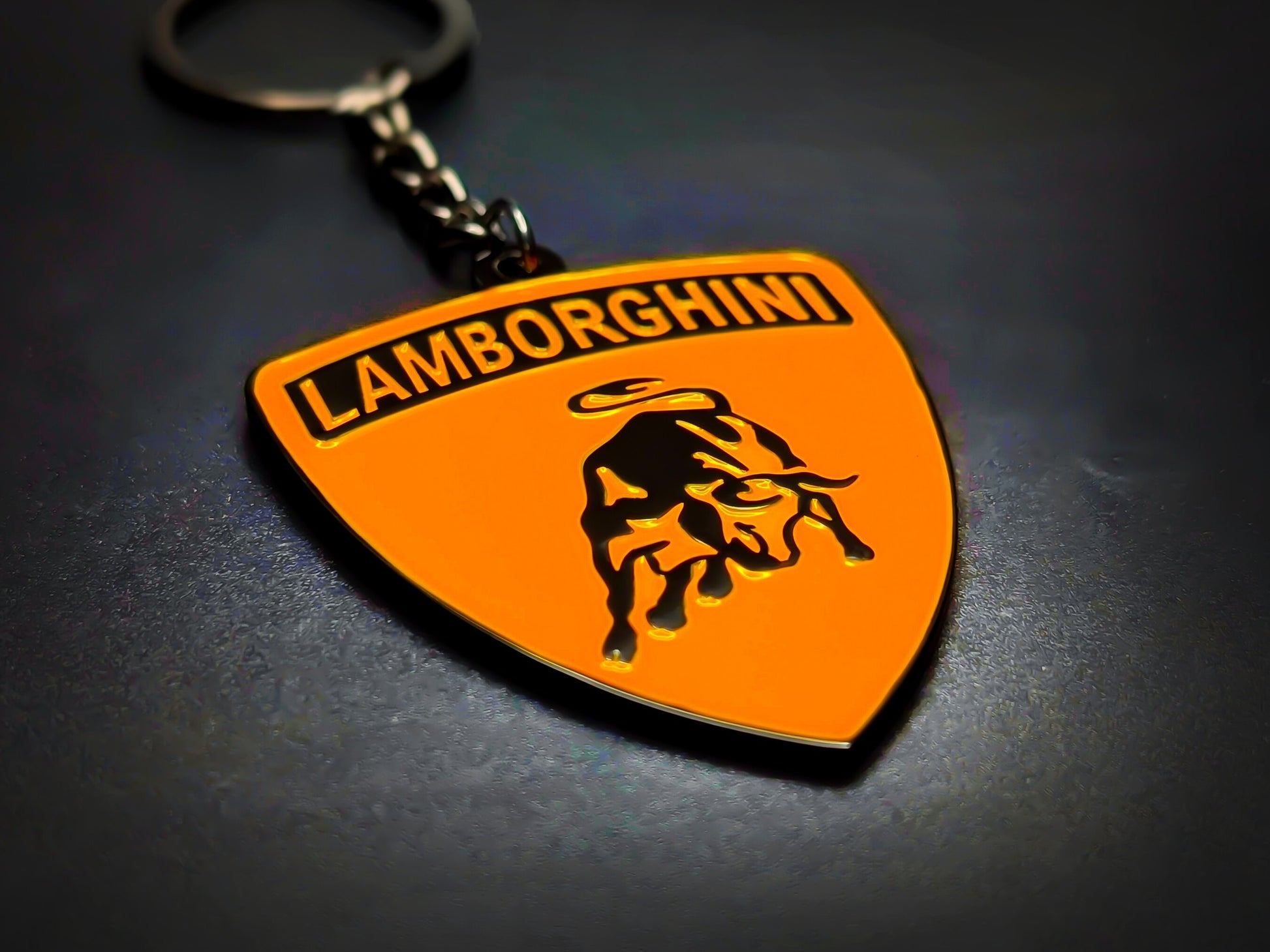 Shield-shaped orange and black Lamborghini metal keychain with a black bull logo and the "Lamborghini" wordmark.