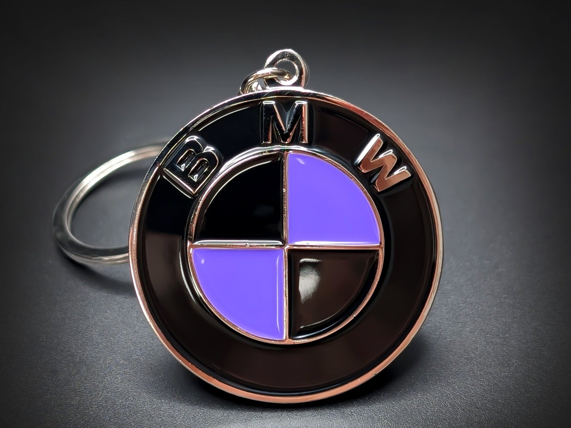 Round black and silver BMW double-sided metal keychain with a purple and black checkered logo and "BMW" text.