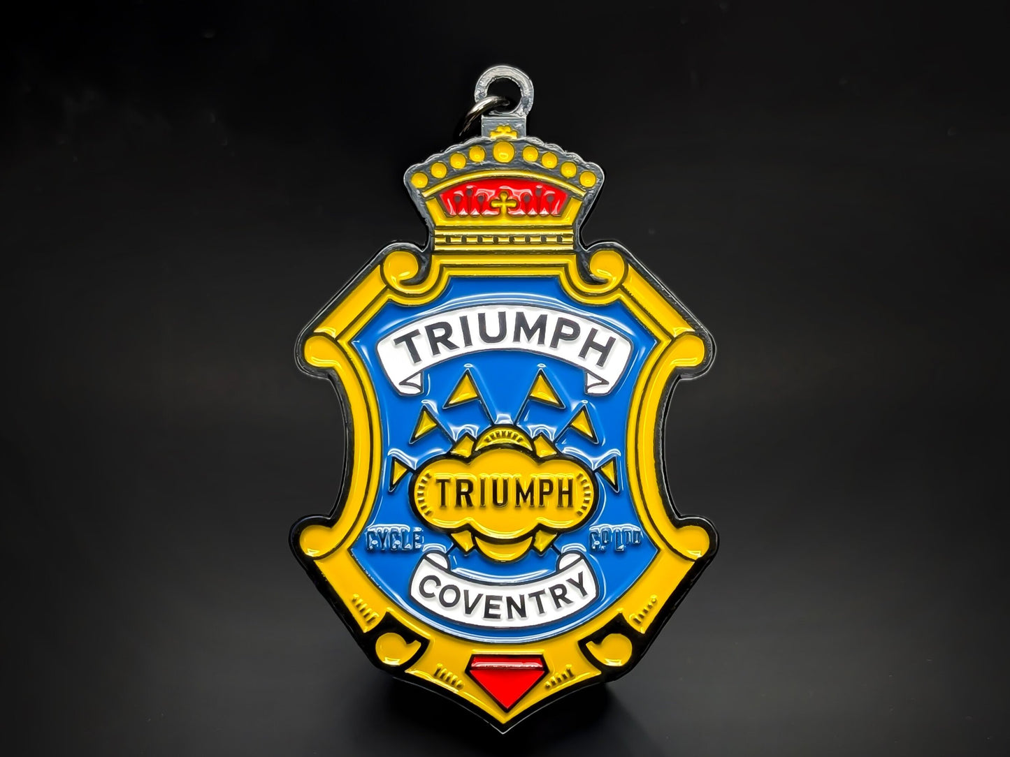 Blue, yellow, and red shield-shaped Triumph metal keychain with a crown, a banner, and the word "COVENTRY."