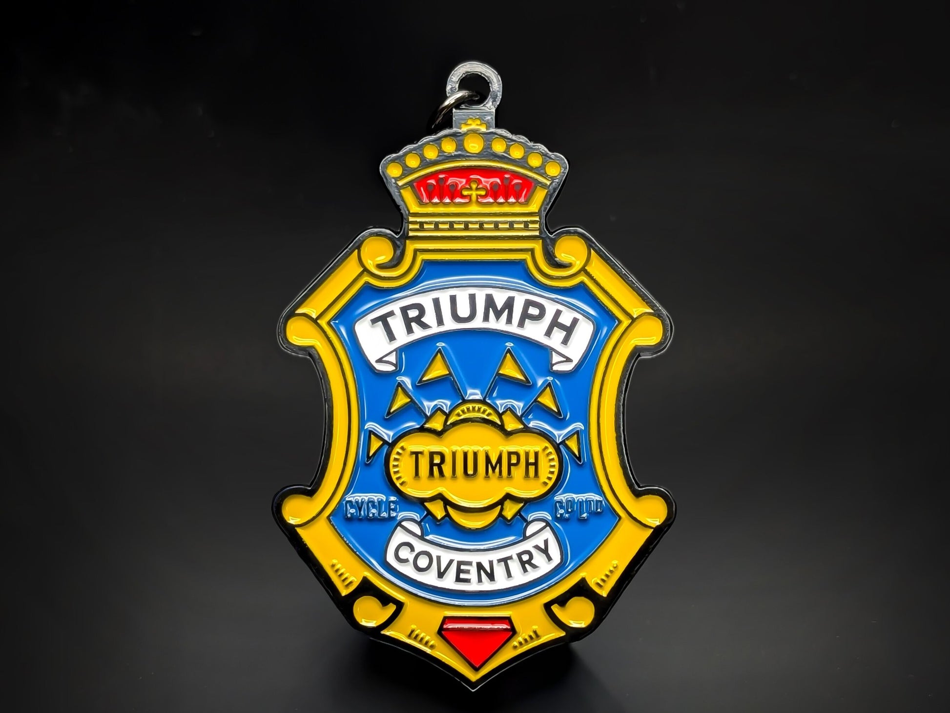Blue, yellow, and red shield-shaped Triumph metal keychain with a crown, a banner, and the word "COVENTRY."