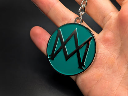 Hand holding a circular Aston Martin AM monogram enamel badge keychain to demonstrate the premium metallic weight and 3D details.