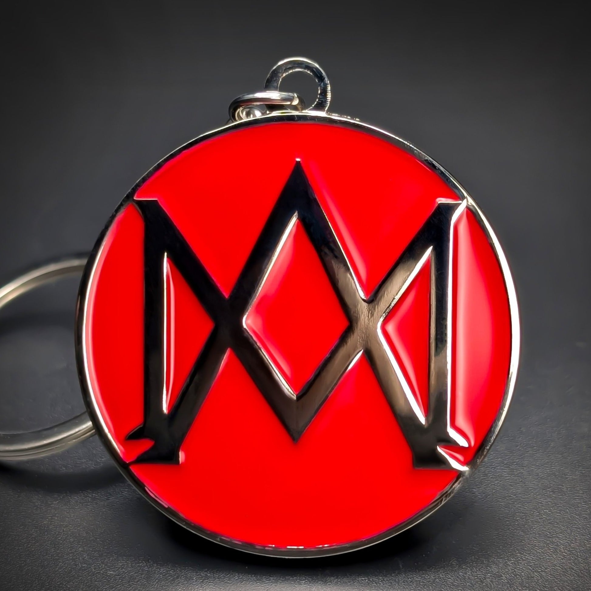 Double-sided metal Aston Martin badge keychain with a black abstract wing emblem on a glossy red enamel background, chrome rim and loop at the top, on a dark gradient surface.