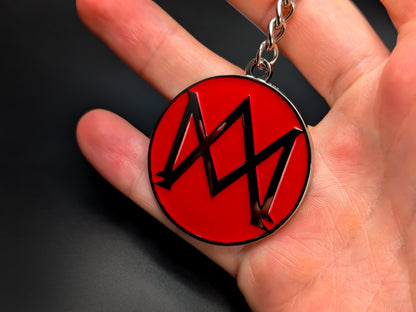 Hand holding a circular Aston Martin AM monogram enamel badge keychain to demonstrate the premium metallic weight and 3D details.