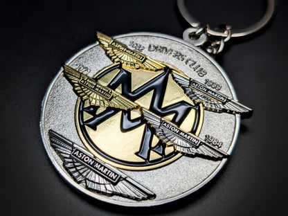 Detailed view of the Aston Martin badge keychain showing the black enamel "AM" logo and tiered metallic wing structure.