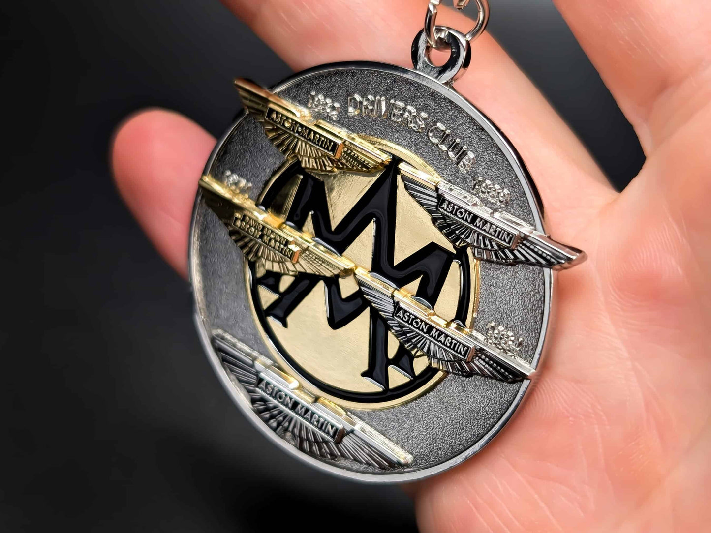 Aston Martin Drivers Club metal badge keychain held in hand to show size, featuring the iconic wings and "Drivers Club" text.