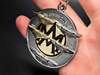 Aston Martin Drivers Club metal badge keychain held in hand to show size, featuring the iconic wings and "Drivers Club" text.