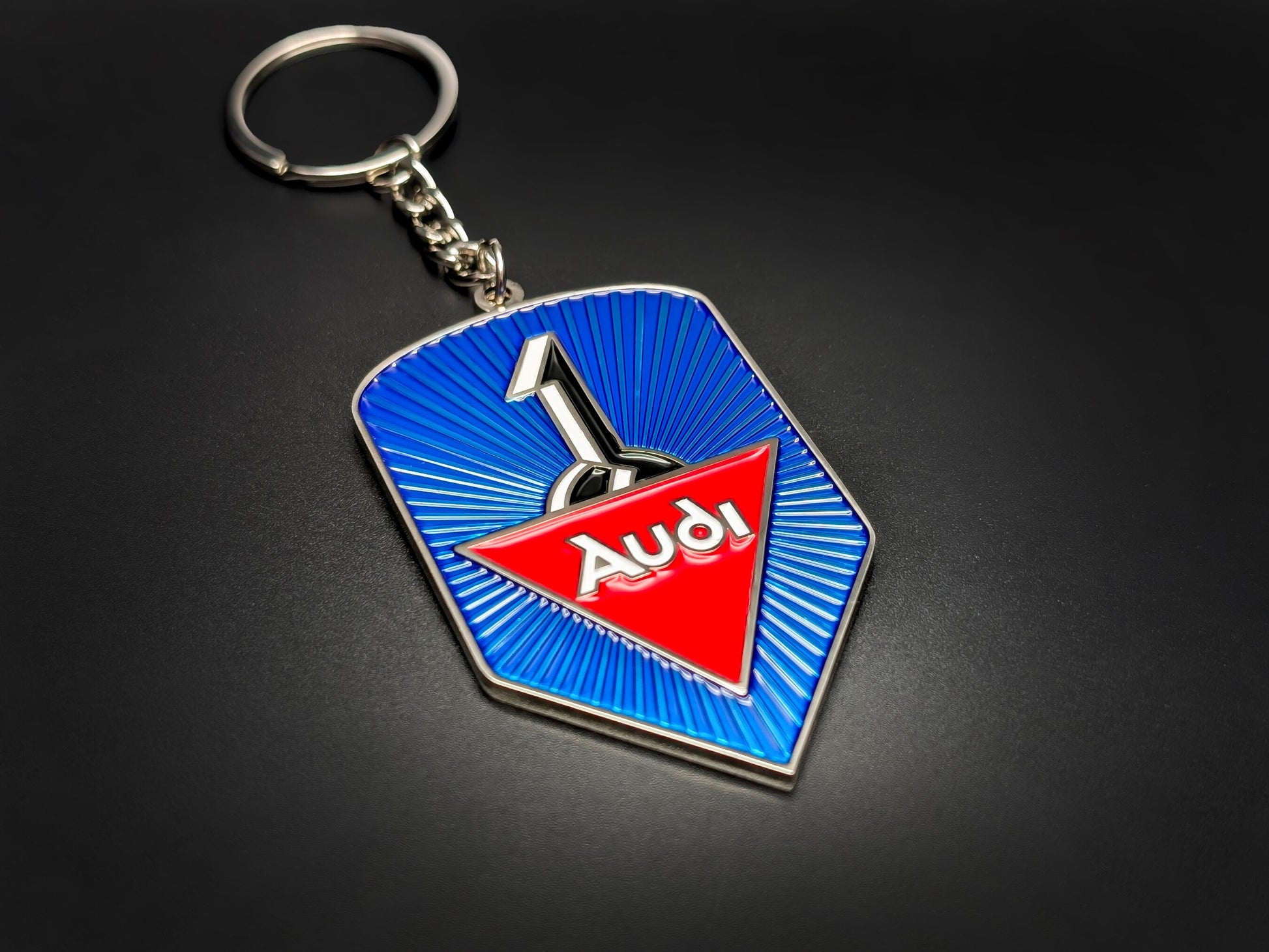 High-quality retro Audi car badge keychain on a dark background, showing the polished silver metal edges and vibrant blue enamel.