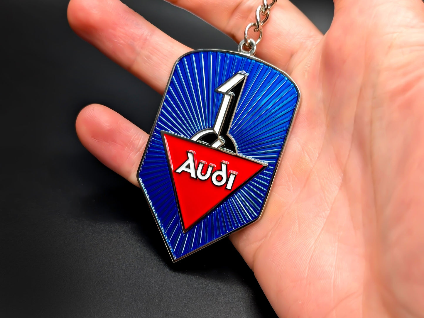Audi heritage badge keychain held in hand to show size, featuring the classic 1930s style logo and premium metal construction.