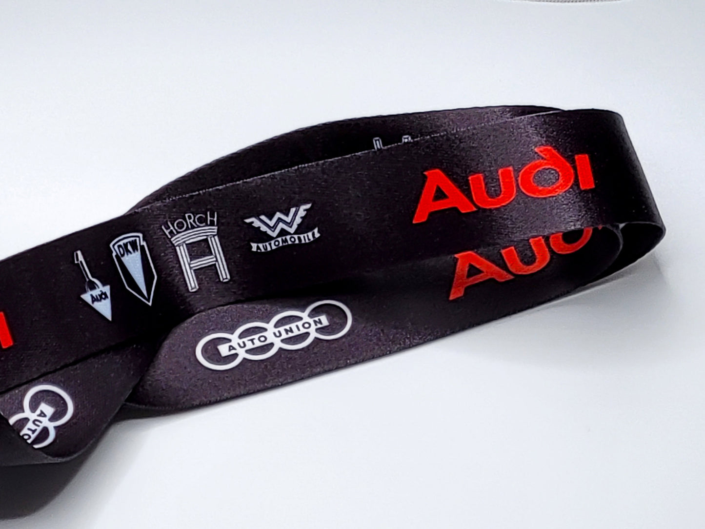 Close-up of a black satin lanyard showing historical Audi brand logos including Horch, Wanderer, and DKW.