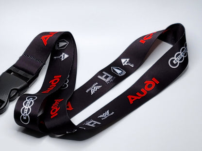 Premium black Audi neck lanyard with repeating red "Audi" text and white vintage automotive heritage symbols.