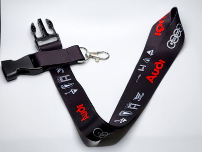 Black automotive lanyard with a quick-release plastic buckle, metal key attachment, and multi-generational Audi branding.