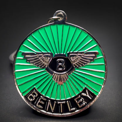 Double-sided metal Bentley badge keychain with silver wings and a silver B on a black shield over green sunburst enamel, BENTLEY lettering on a black band, silver split ring, on a dark surface.