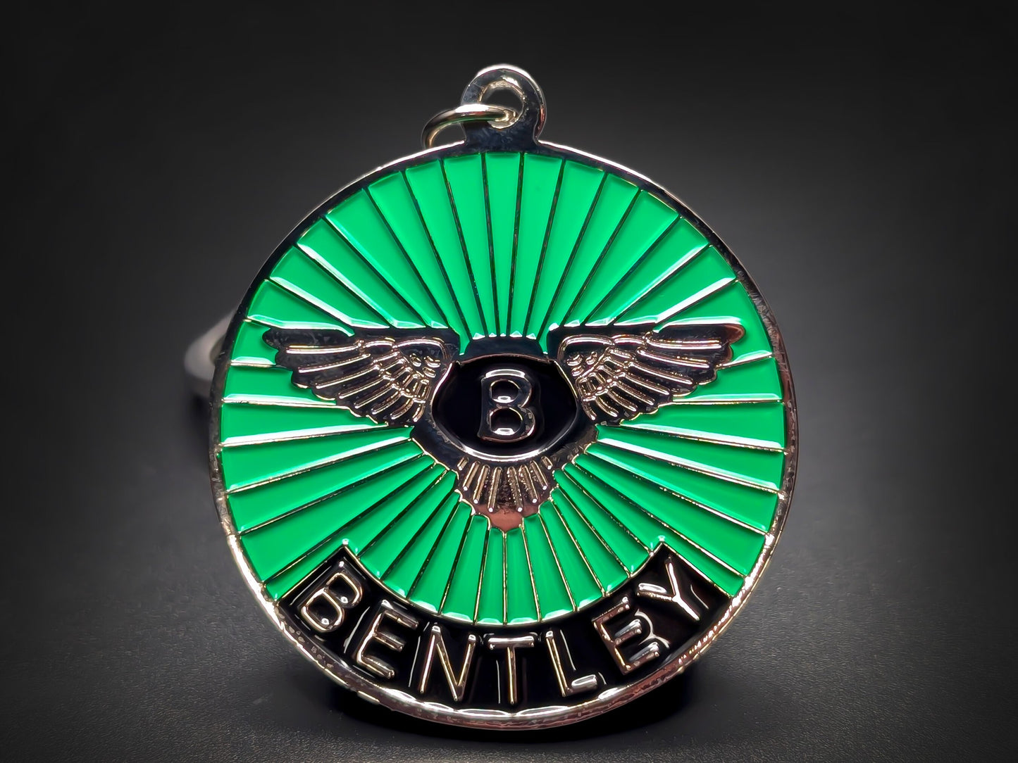 Close-up shot of a circular metal badge keychain featuring the Bentley winged emblem on a vibrant green sunburst enamel background.