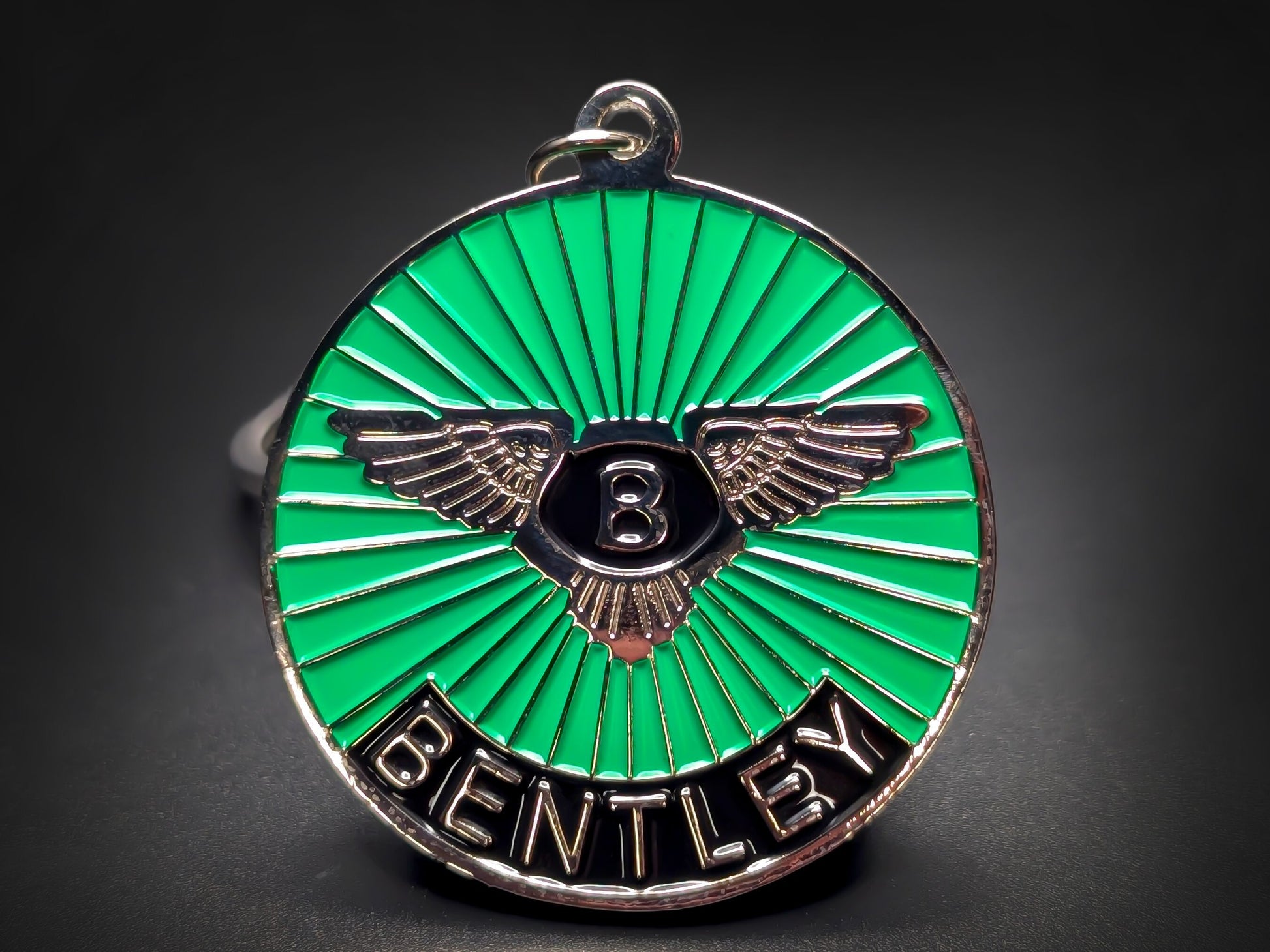 Close-up shot of a circular metal badge keychain featuring the Bentley winged emblem on a vibrant green sunburst enamel background.