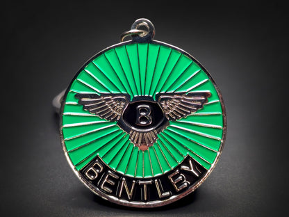 Close-up shot of a circular metal badge keychain featuring the Bentley winged emblem on a vibrant green sunburst enamel background.