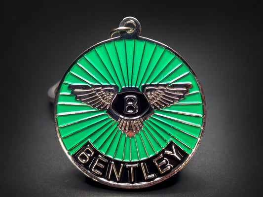 Close-up shot of a circular metal badge keychain featuring the Bentley winged emblem on a vibrant green sunburst enamel background.