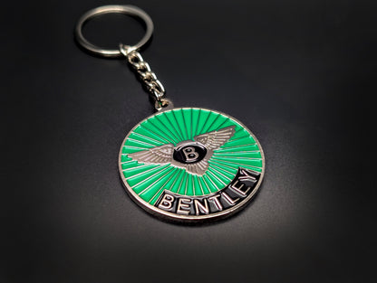 A green Bentley sunburst badge keychain with a silver chain and ring, showcased against a smooth dark background.