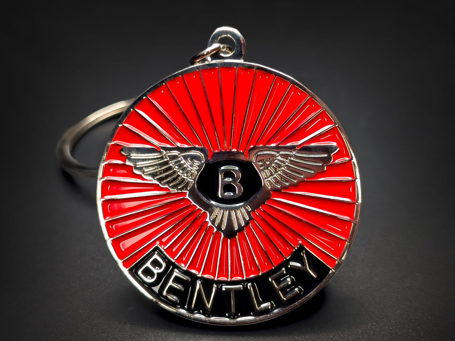 Close-up of a circular metal badge keychain featuring the Bentley winged logo over a vibrant red sunburst enamel background.