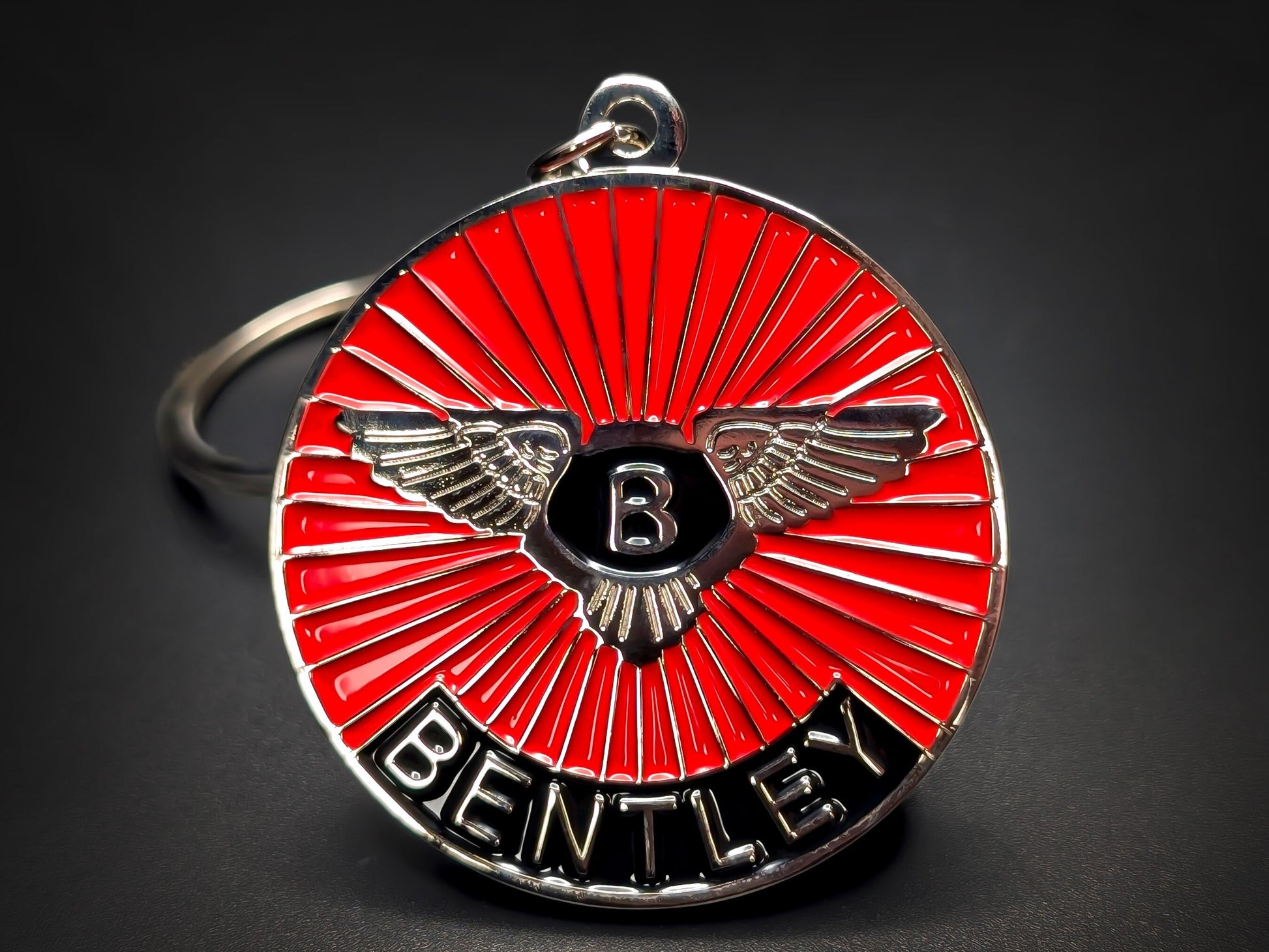 Close-up of a circular metal badge keychain featuring the Bentley winged logo over a vibrant red sunburst enamel background.