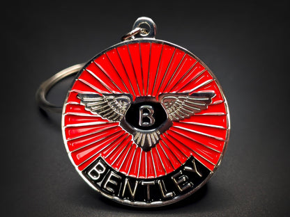 Close-up of a circular metal badge keychain featuring the Bentley winged logo over a vibrant red sunburst enamel background.