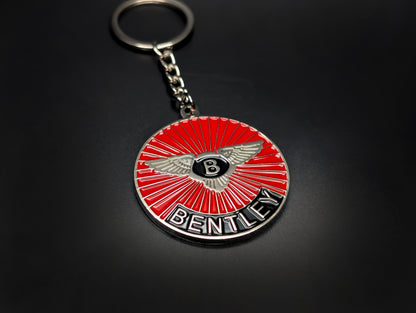 A Bentley red sunburst badge keychain with a silver link chain and keyring, displayed on a sleek dark surface.