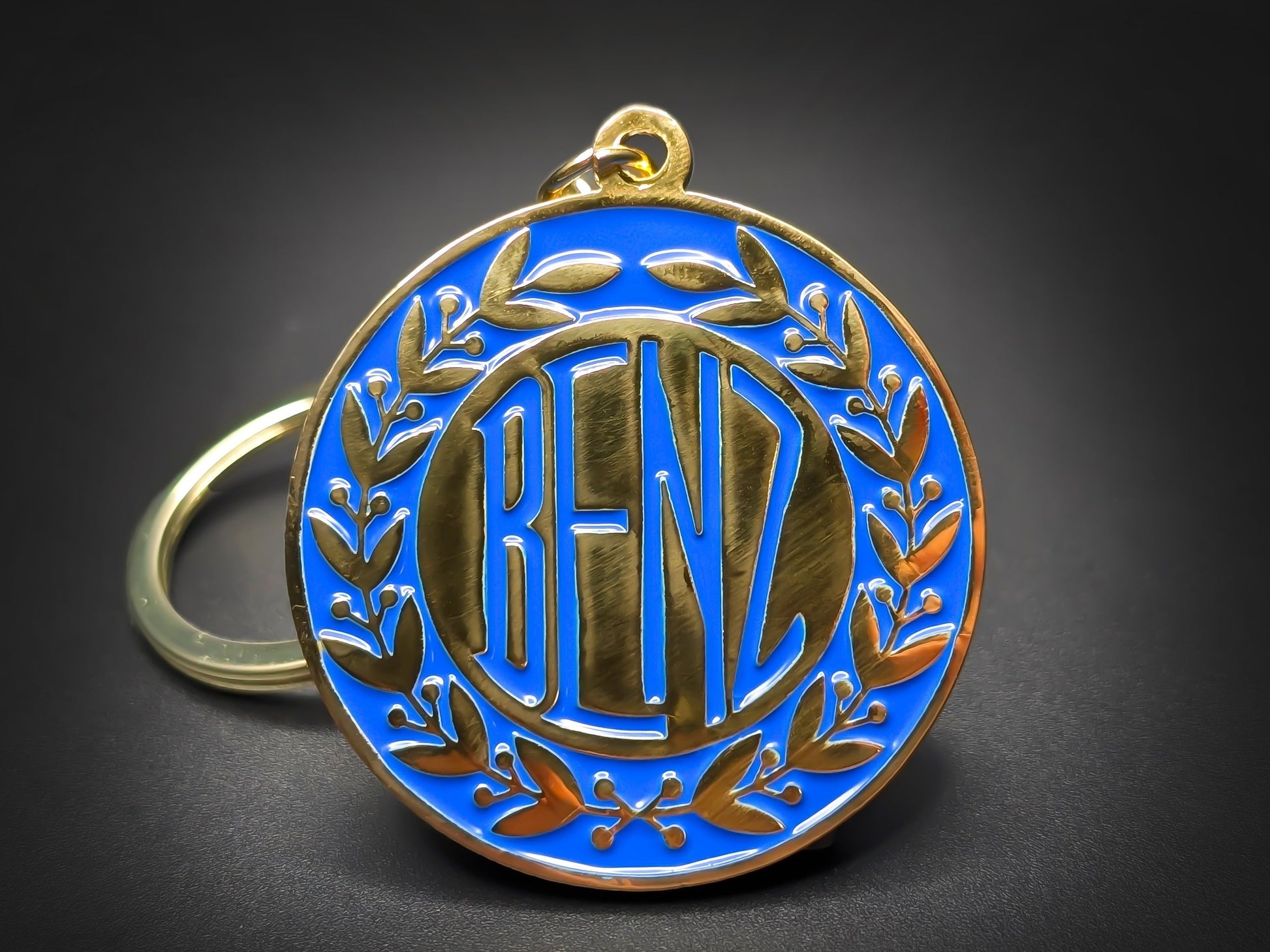 Vintage Benz badge keychain featuring gold 1909 lettering and a laurel wreath on a vibrant blue enamel circular base.