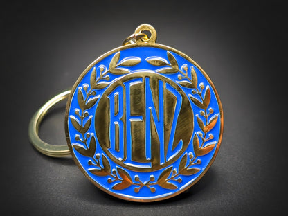 Vintage Benz badge keychain featuring gold 1909 lettering and a laurel wreath on a vibrant blue enamel circular base.